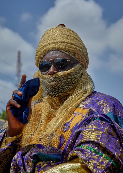 Free Portrait of a man in vibrant traditional attire and sunglasses standing outdoors under a blue sky. Stock Photo