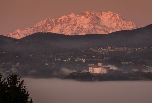 Free Stunning sunset view of a castle beneath towering mountains in Italy with misty foreground. Stock Photo
