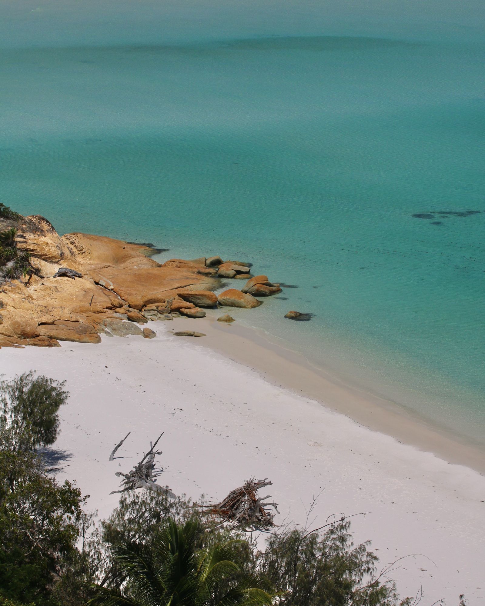 White sand beach with orange shoreline rocks meeting clear turquoise water in the Whitsunday Islands