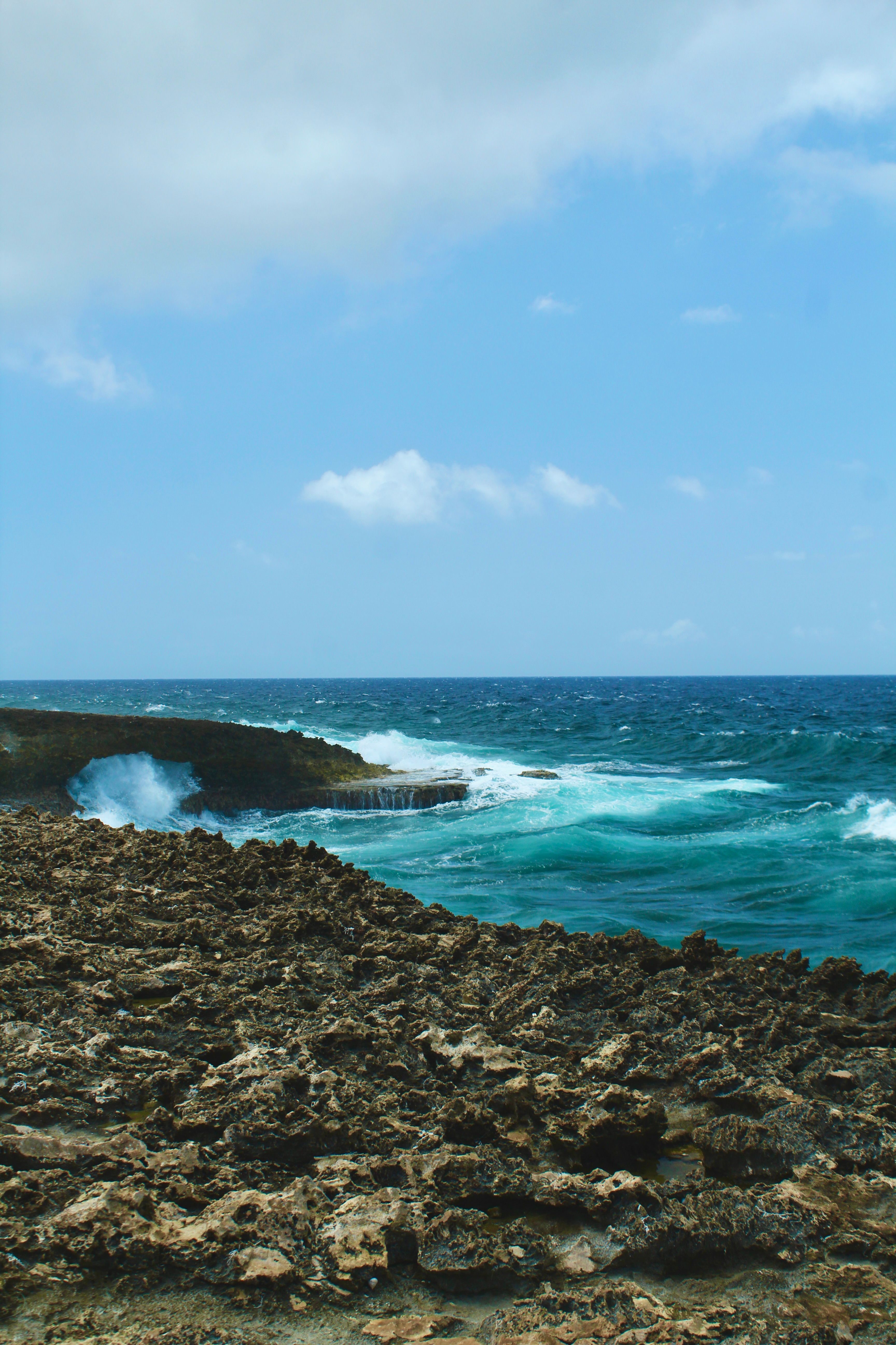 Stunning view of the rocky coastline and ocean waves in Willemstad, Curaçao, under a bright blue sky.