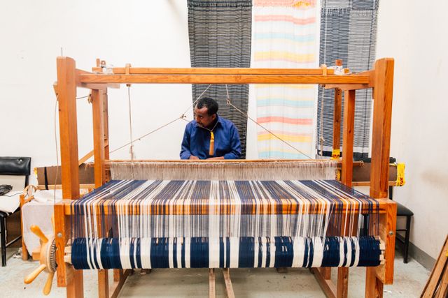 A weaver seated at a four-shaft floor loom with a striped warp, photo by K on Pexels