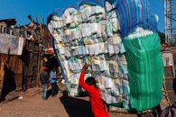 Side view of anonymous ethnic male in casual wear carrying heavy stack of merchandise with striped bags on dry terrain under blue sky in sunlight