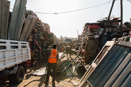Unrecognizable workmen standing near pile of metal scrap in dump