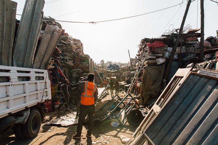 Unrecognizable Workmen Standing Near Pile Of Metal Scrap In Dump