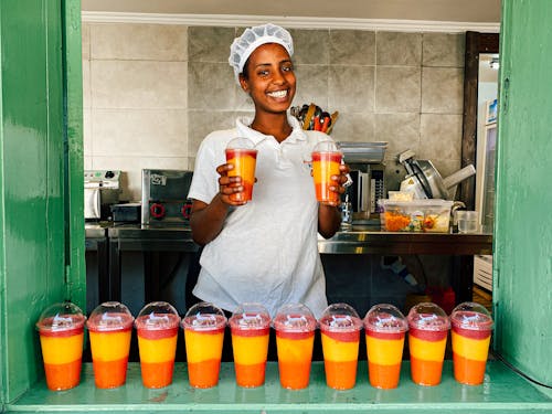 Woman in White Polo Shirt Holding Multicolored Shake in Plastic Cups