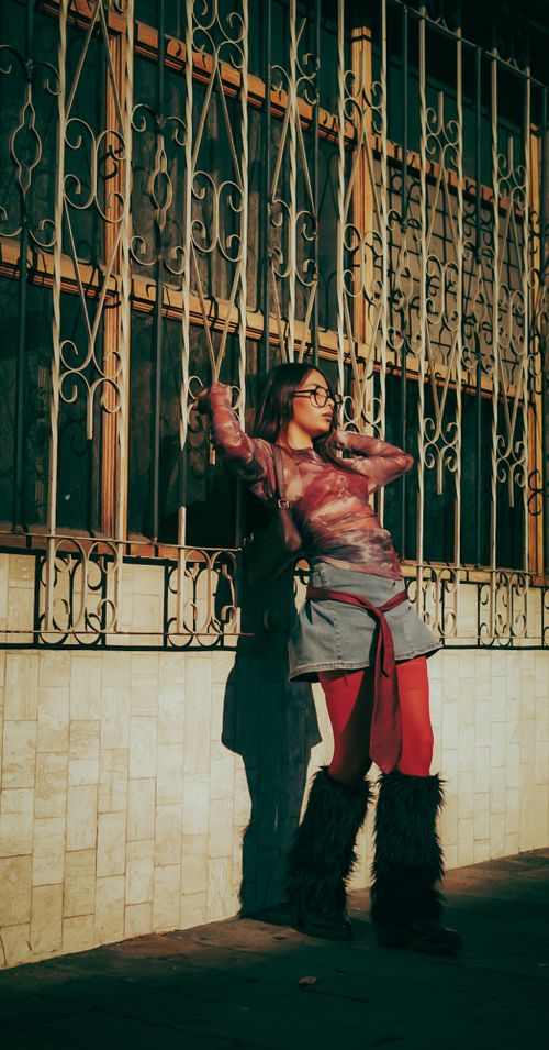 Free Stylish woman in vibrant attire poses by ornate fence, capturing light and shadow contrast. Stock Photo