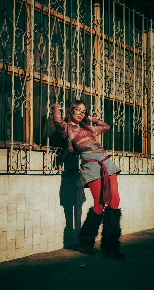 Free A fashionable woman stands confidently against an ornate iron grate, showcasing urban style and attitude. Stock Photo