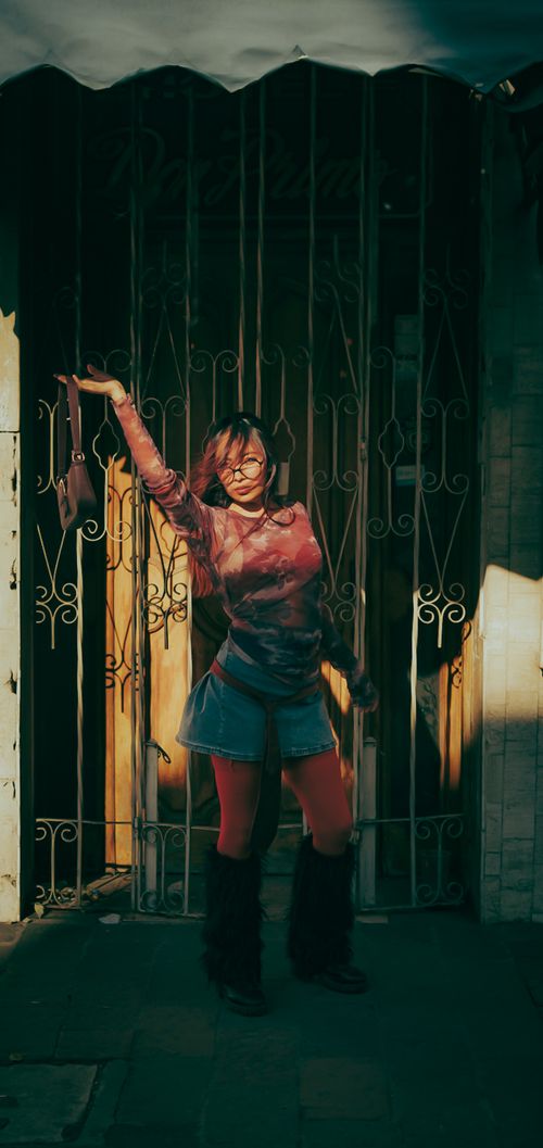 Free A stylish woman confidently poses against an ornate iron gate, basking in warm sunlight. Stock Photo