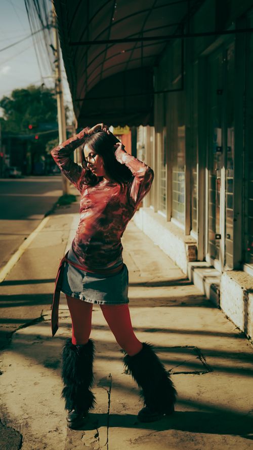 Free Fashionable woman posing in sunlight on city sidewalk, showcasing vibrant street style. Stock Photo