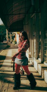 Fashionable woman in red tights and fur boots poses on a sunny city sidewalk.