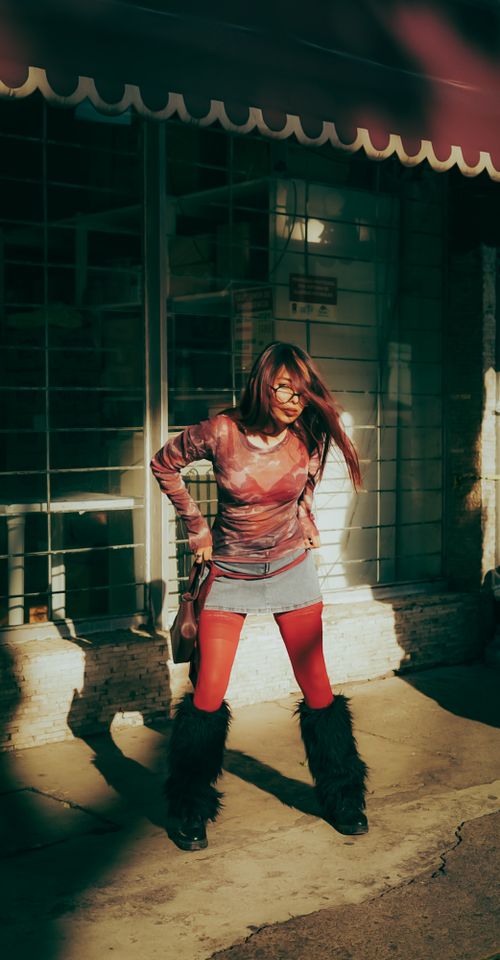 Free Stylish woman in red tights and urban attire posing in sunlight outside storefront. Stock Photo