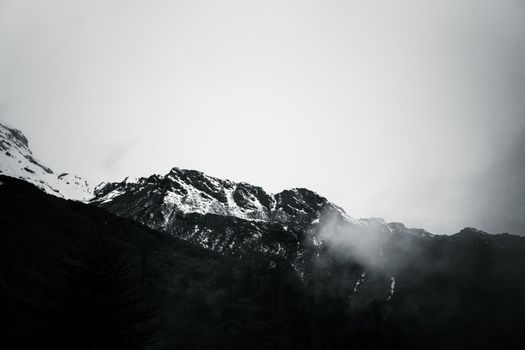 A dramatic view of snow-covered mountains shrouded in mist, evoking a moody atmosphere.