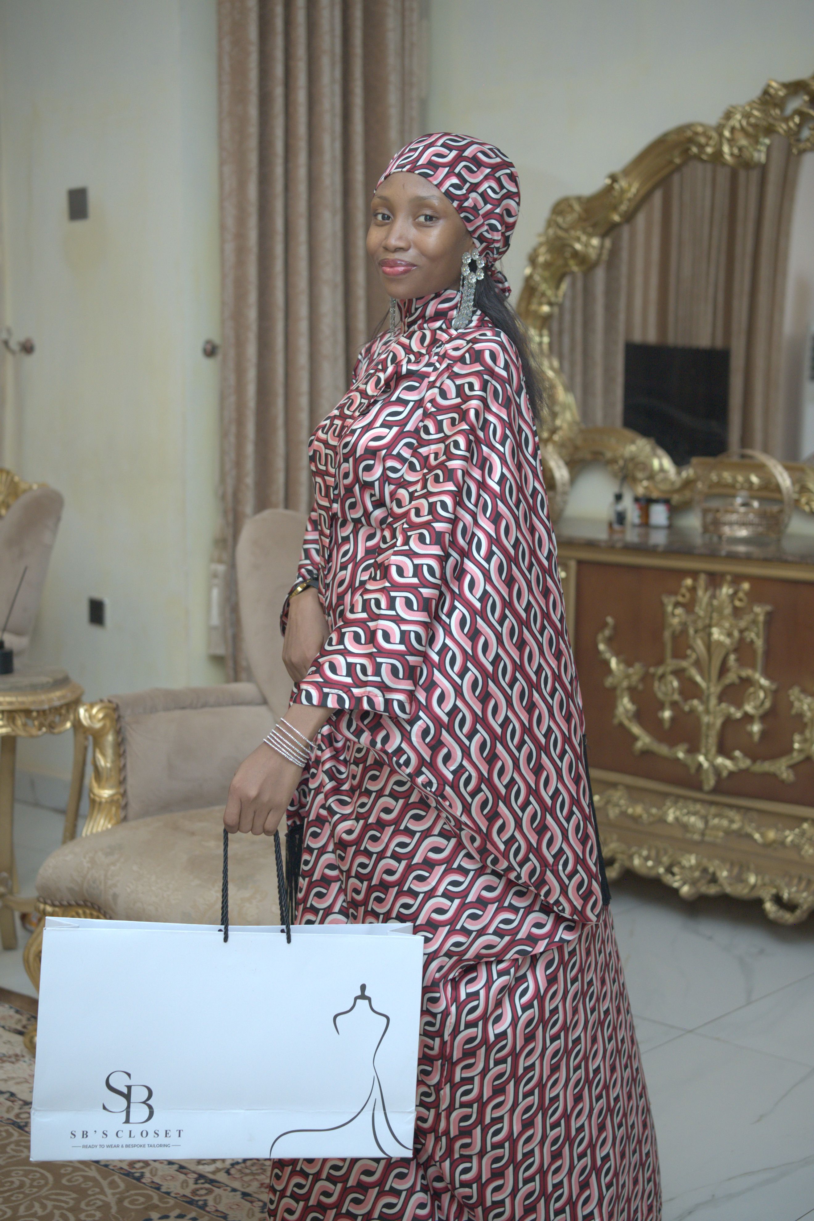 Woman in Sokoto, Nigeria wearing patterned dress holding shopping bag indoors.