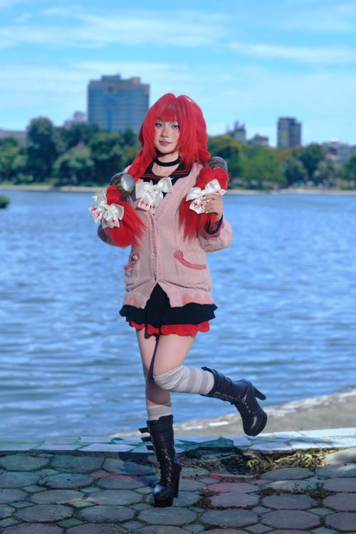 Free Cosplayer in vibrant costume posing by a lakeside in a cityscape backdrop. Stock Photo