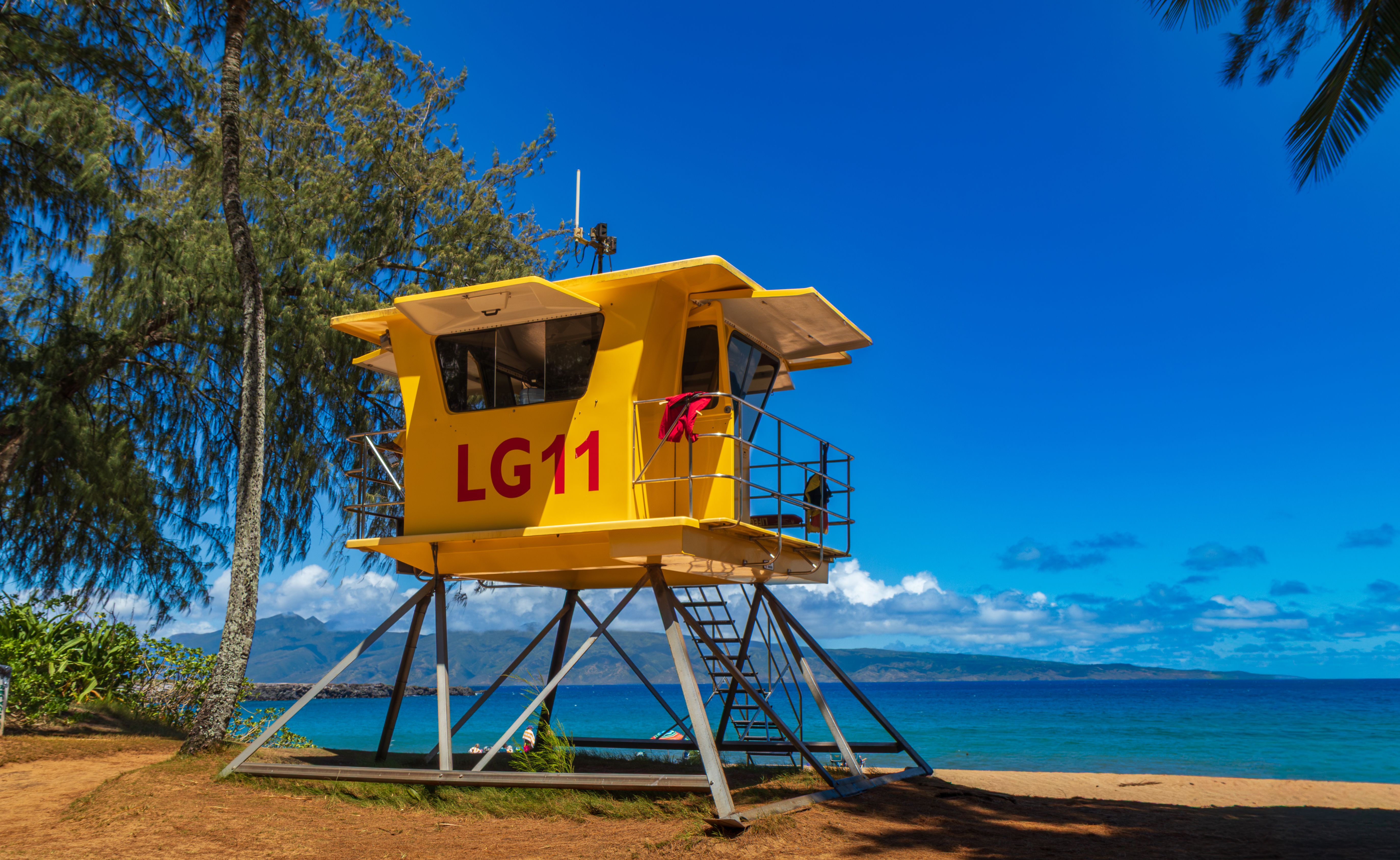 Bright yellow lifeguard tower against a vibrant blue Hawaiian sky and ocean, Kapalua.