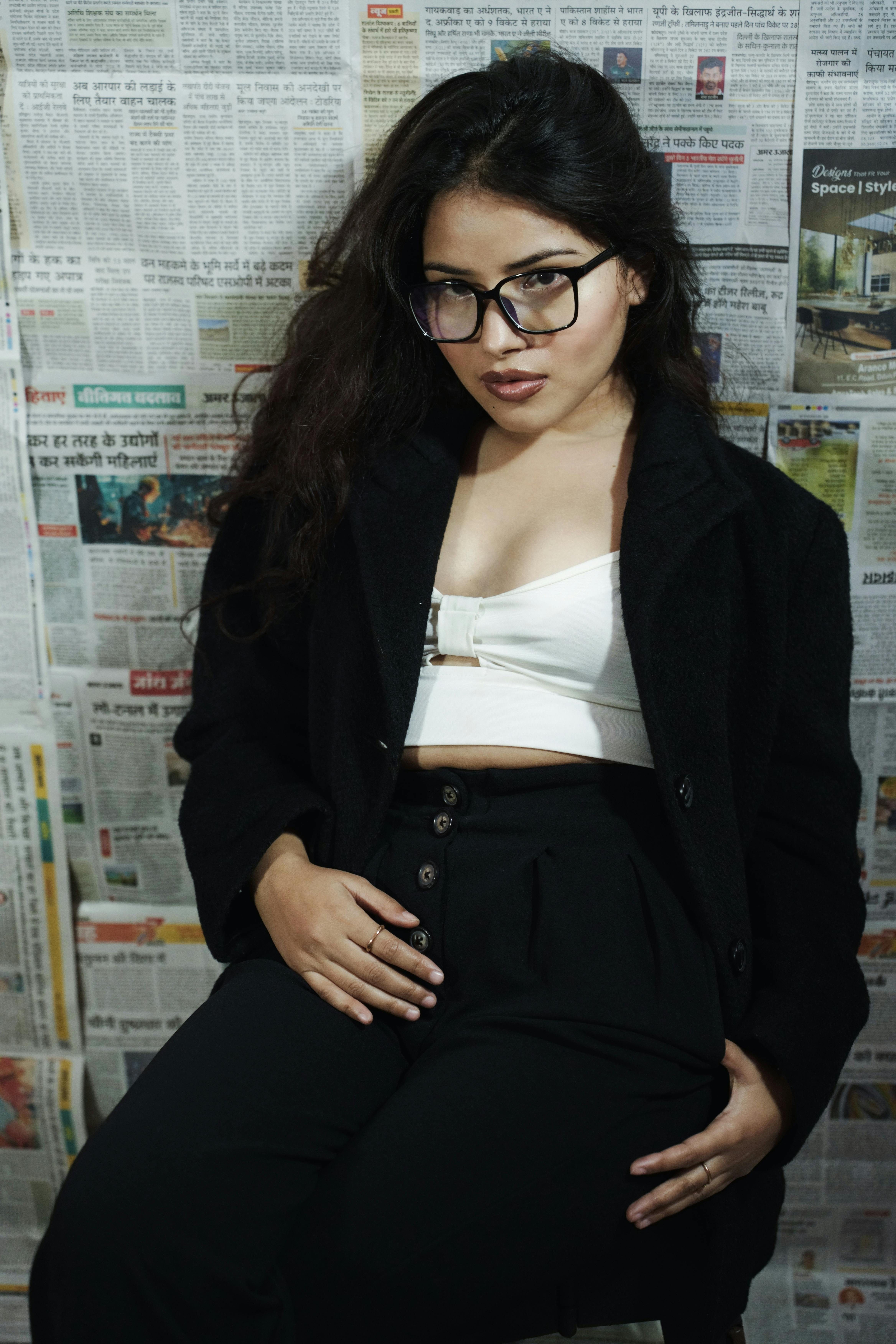 Stylish woman posing indoors in fashionable black and white attire with newspaper background.