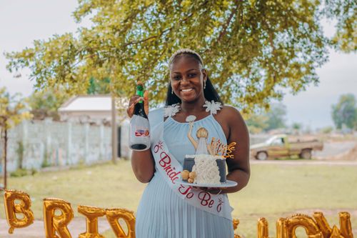 Free An outdoor bridal shower with a smiling bride-to-be holding a cake and champagne. Stock Photo