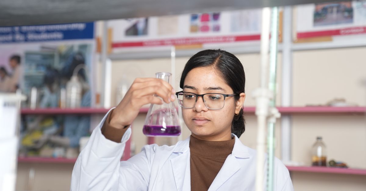Female scientist examining a purple chemical solution in a laboratory setting.
