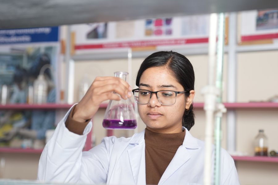 Female scientist examining a purple chemical solution in a laboratory setting.
