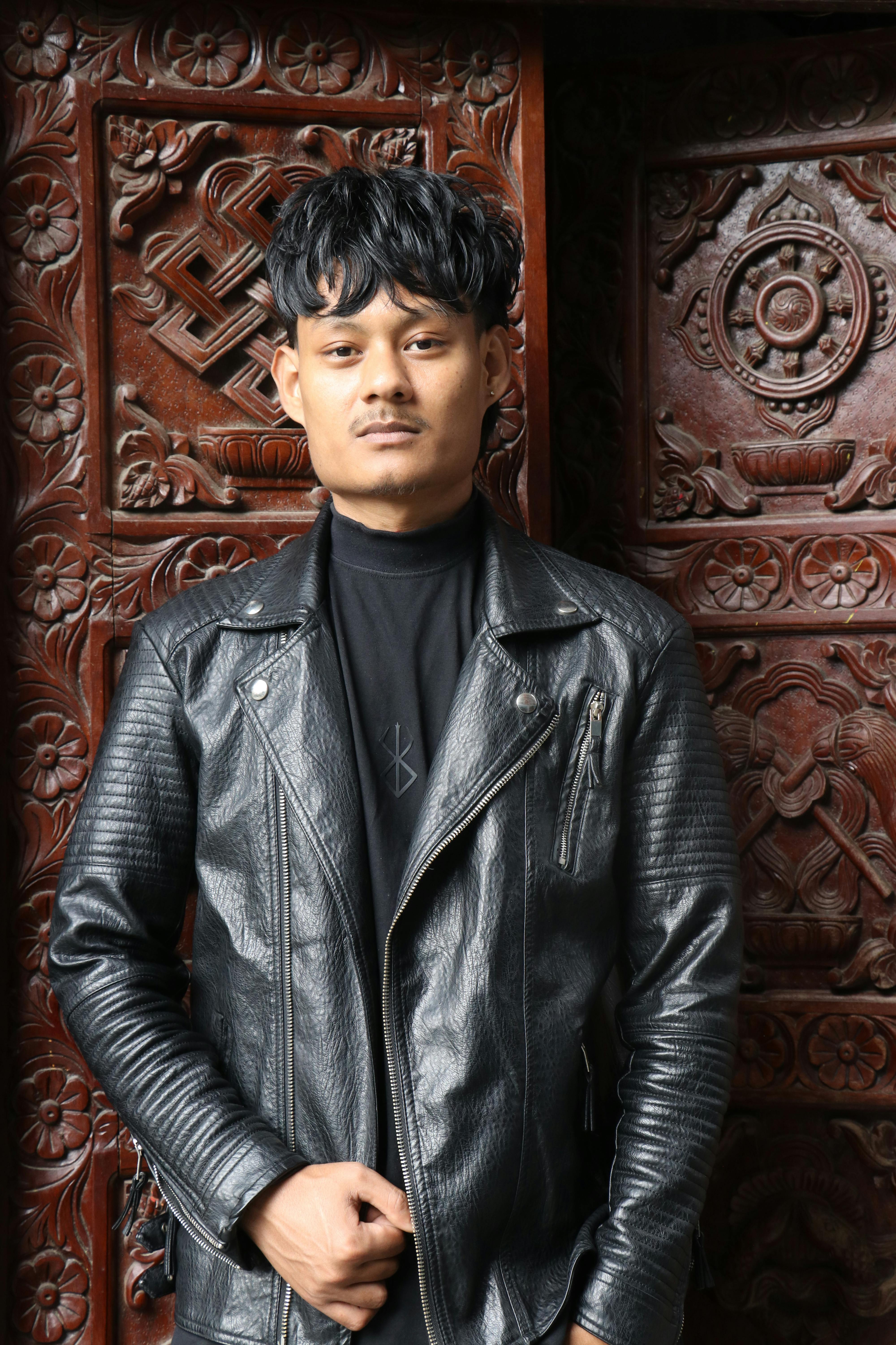 Portrait of a young man in a leather jacket in front of ornate wooden door in Kathmandu, Nepal.