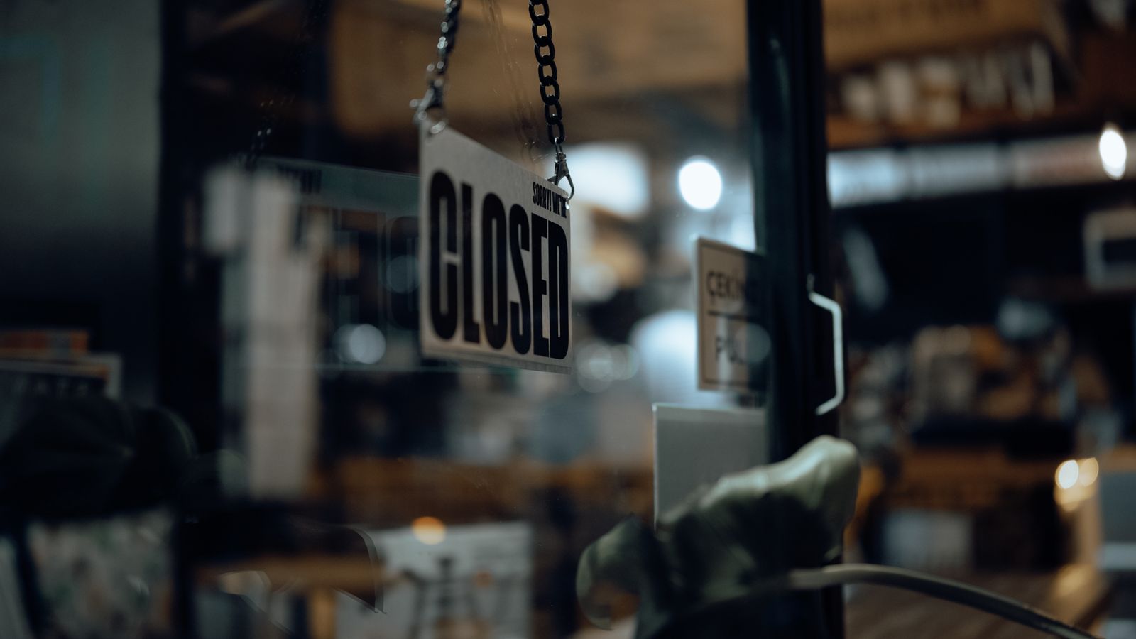 Close-up of a closed sign hanging on a glass door at night, with blurred indoor view.