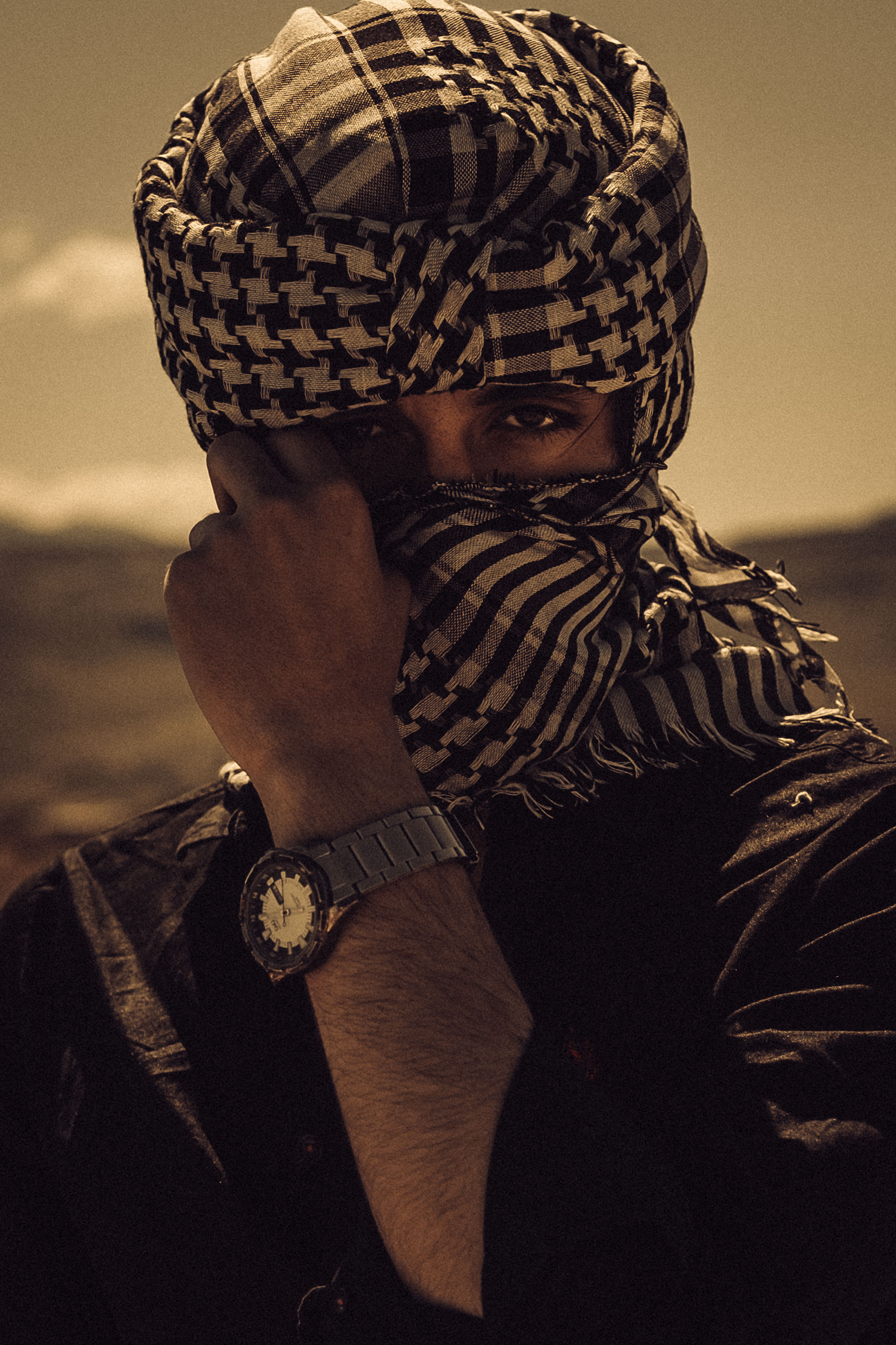 Mysterious individual wearing traditional scarf covers face in desert setting.