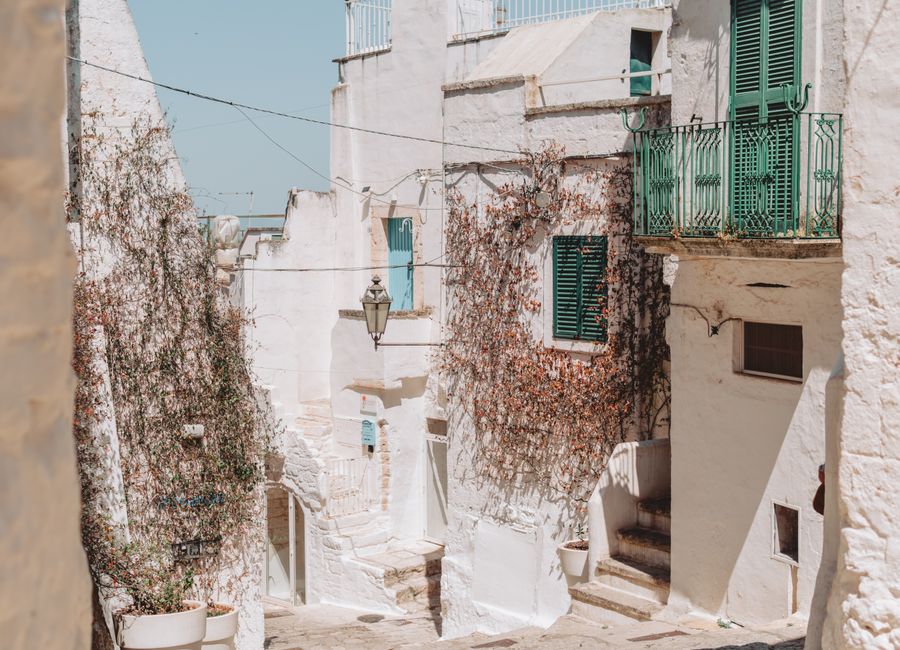 Explore the picturesque alleys of Ostuni, Apulia, with sunlit whitewashed buildings and green shutters.