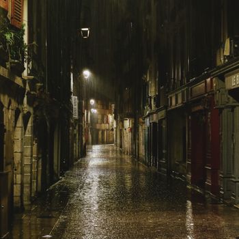 Moody night street scene in Bayonne, France with rain glistening on empty cobblestone street.