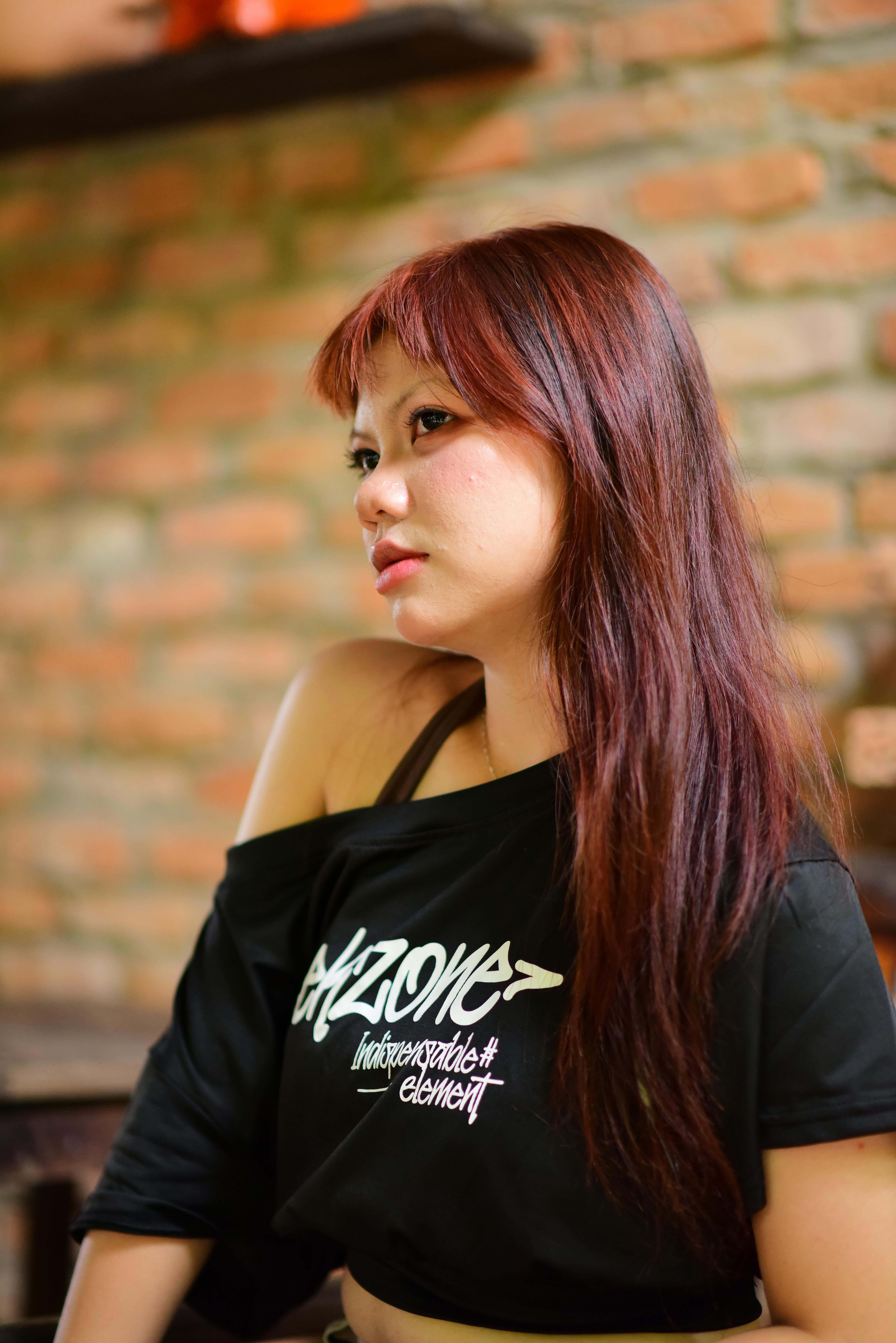 A portrait of a woman with long hair against a rustic brick wall in a relaxed pose.
