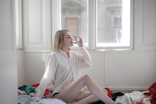 Woman in White Long Sleeve Shirt While Drinking Water