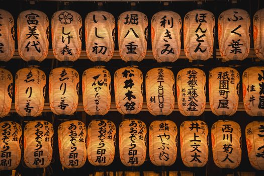 A display of glowing Japanese paper lanterns with kanji characters set against a dark background.