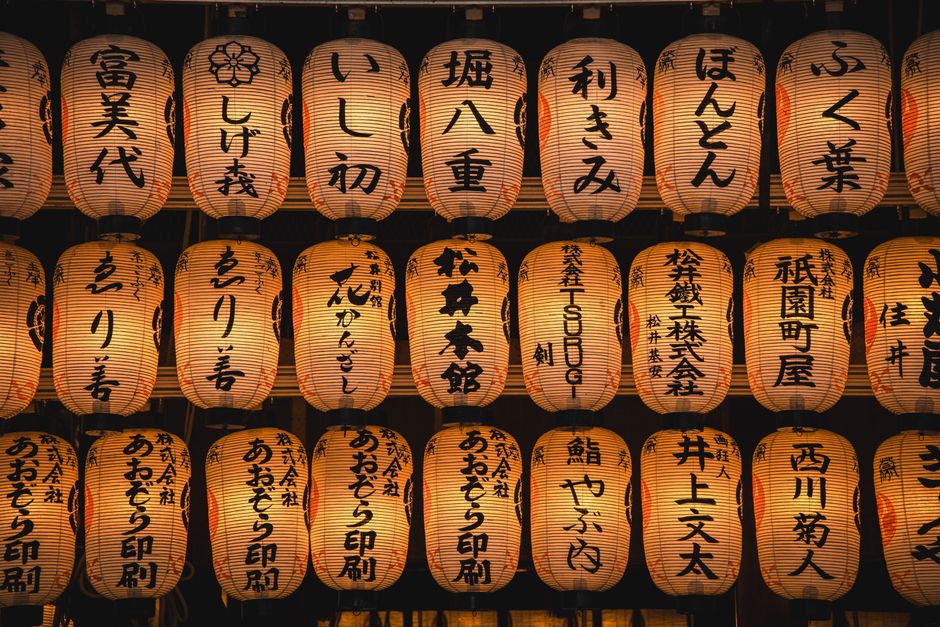 A display of glowing Japanese paper lanterns with kanji characters set against a dark background.