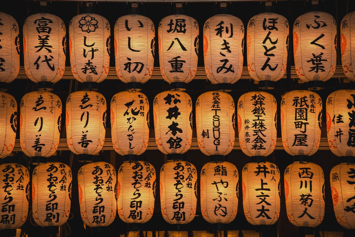 A display of glowing Japanese paper lanterns with kanji characters set against the night, evoking the illuminated spectacle of the Nebuta parade