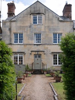 Front view of a classic Georgian-style house surrounded by greenery in Cirencester, UK.