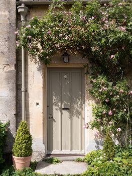 A quaint cottage door in Cirencester, framed by blooming roses and foliage.