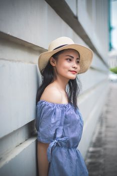 一位长发戴帽的年轻女子倚墙而立，尽显夏日优雅
