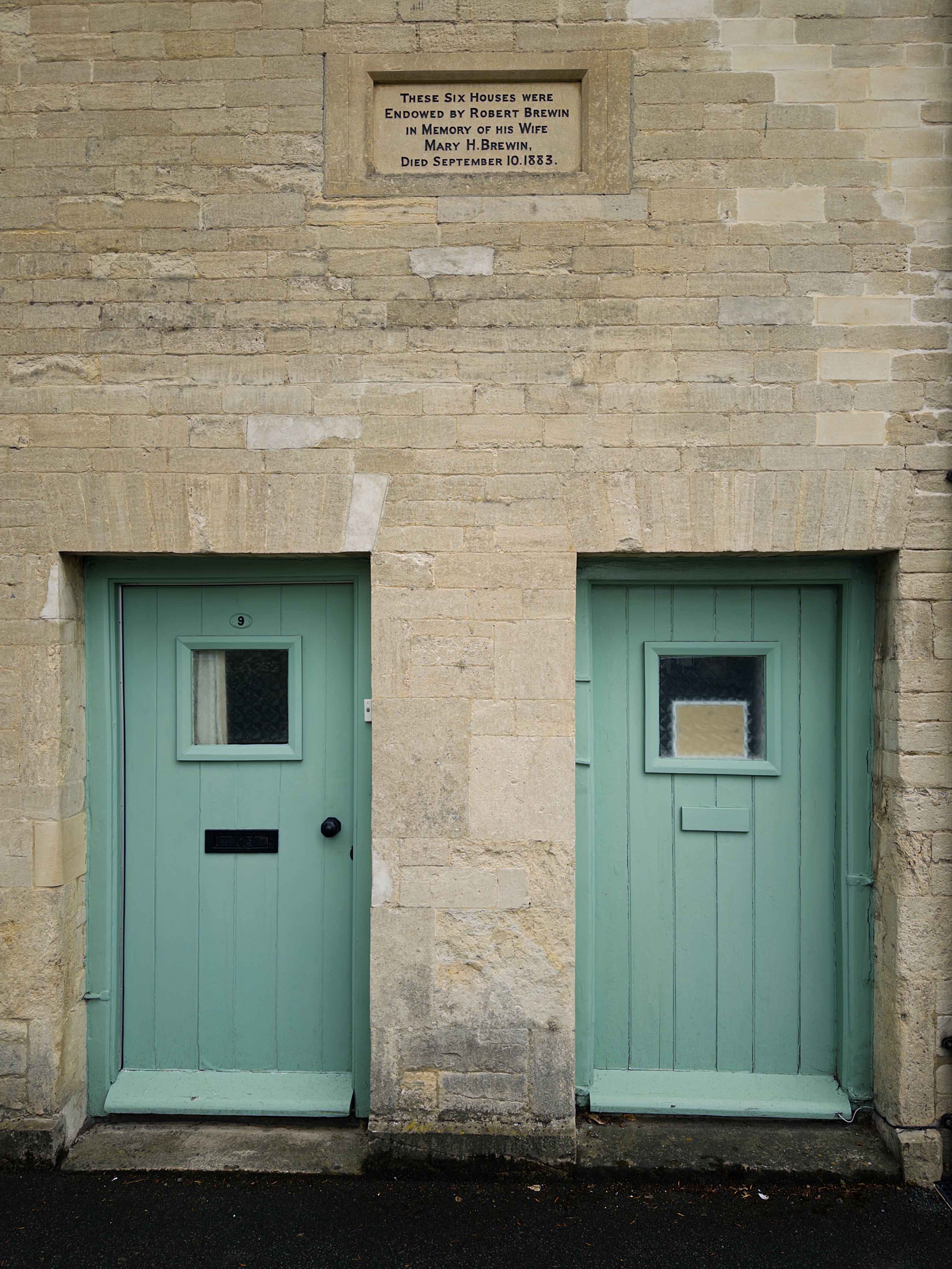 Cotswold stone facade with teal doors in Fairford, Oxfordshire. Historic plaque visible.