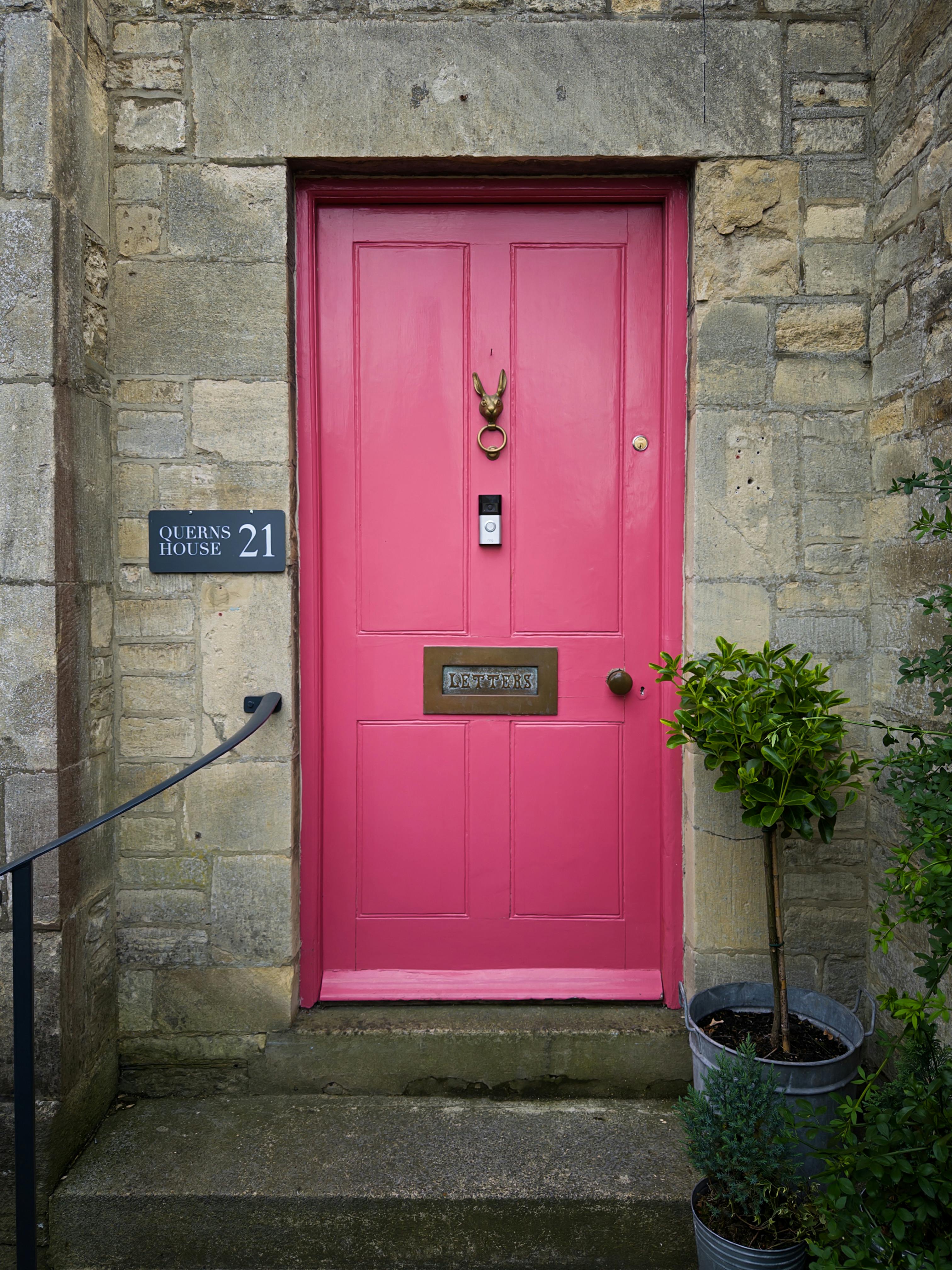 Vibrant pink door on a stone building with unique knocker and plants.