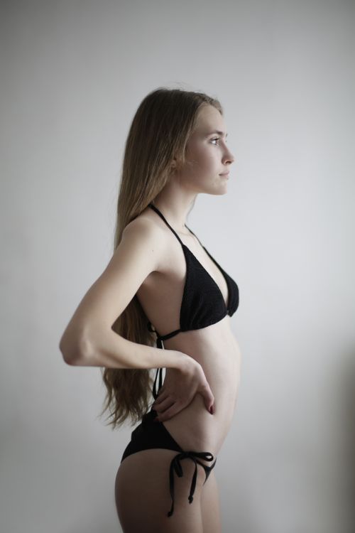 Free Side view of sensual young female model in black swimsuit standing with hands on waist and posing in studio on gray background Stock Photo