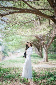 一位身着白色连衣裙、头戴遮阳帽的女子，优雅地站在茂密的树枝下