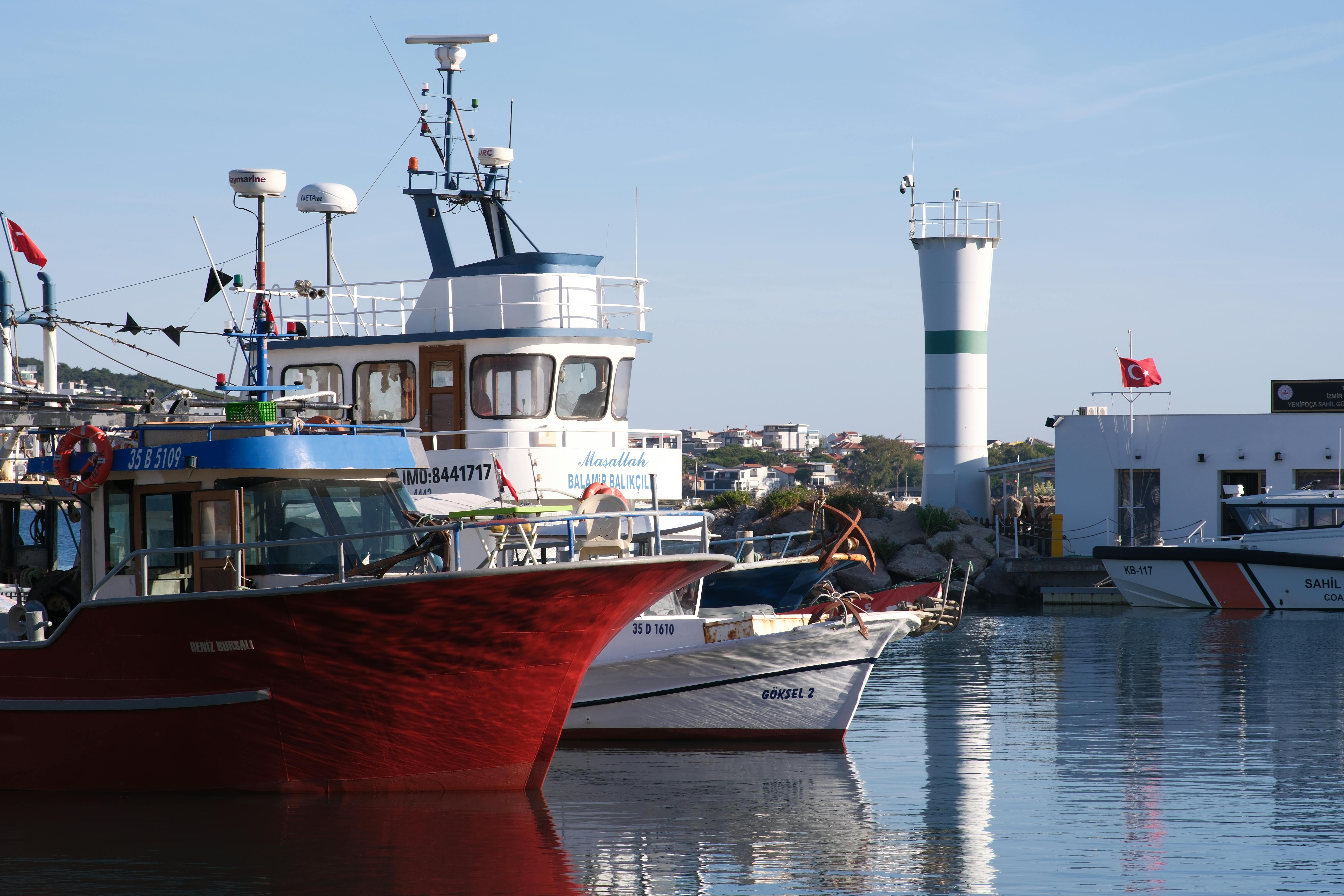 Colorful fishing boats docked at Foça Harbor in İzmir, Türkiye, with a lighthouse in the background.