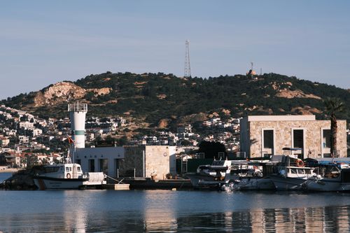Free Idyllic harbor scene in Foça, İzmir with boats and hills under a clear sky. Stock Photo