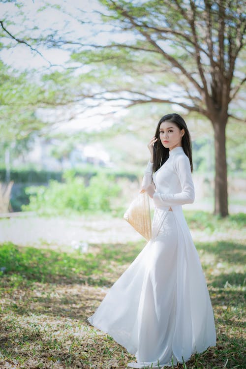 Free Woman in White Long Sleeve Dress Standing on Grass Field Stock Photo