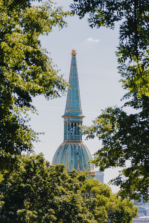 Free A breathtaking view of a historical church steeple framed by lush green trees in Bratislava. Stock Photo