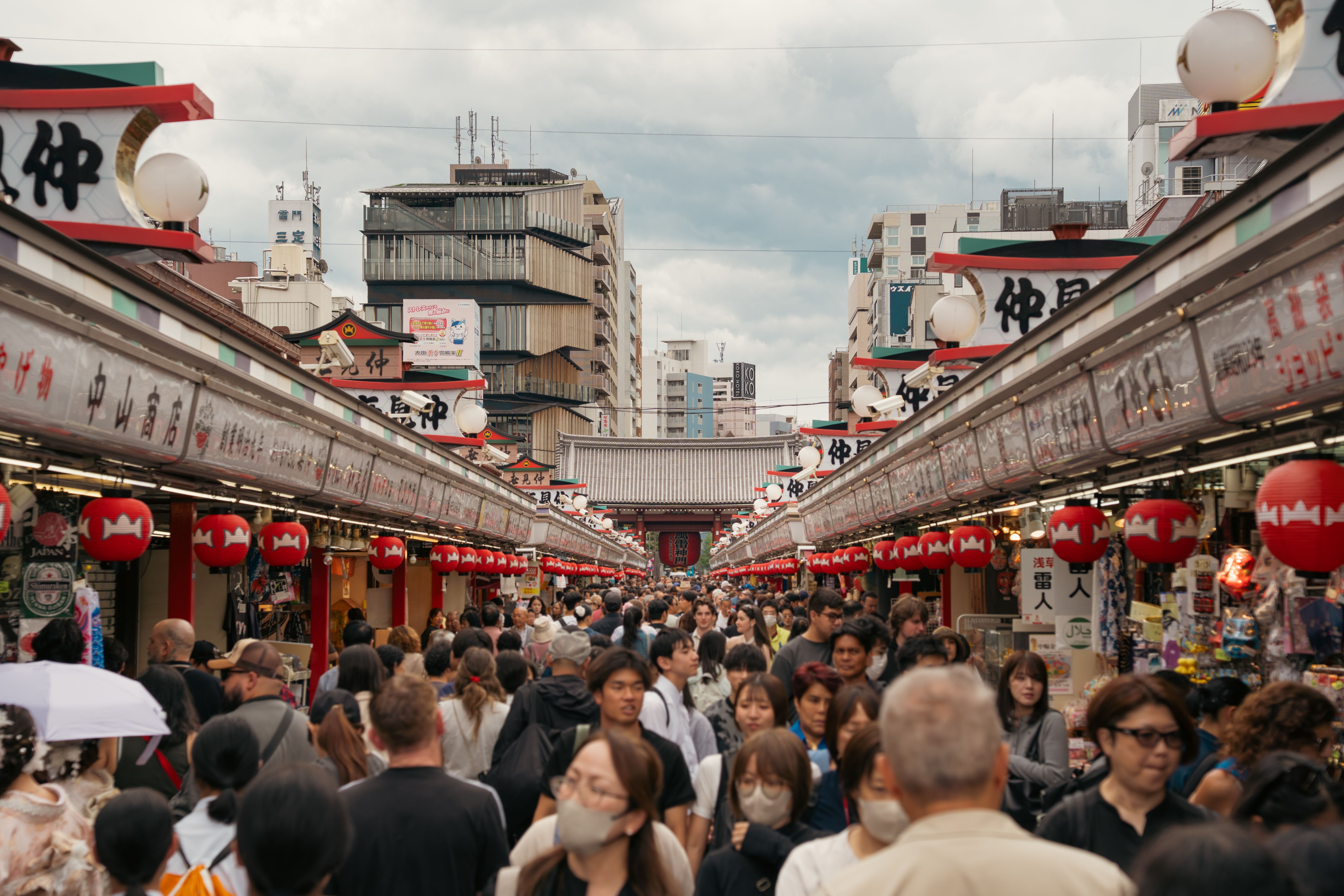 Vibrant street market in Asakusa, Tokyo with red lanterns and bustling crowd.