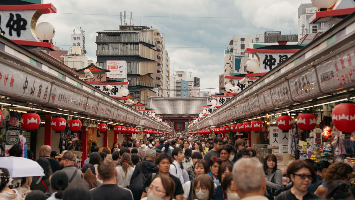 Vibrant street market in Asakusa, Tokyo with red lanterns and bustling crowd.