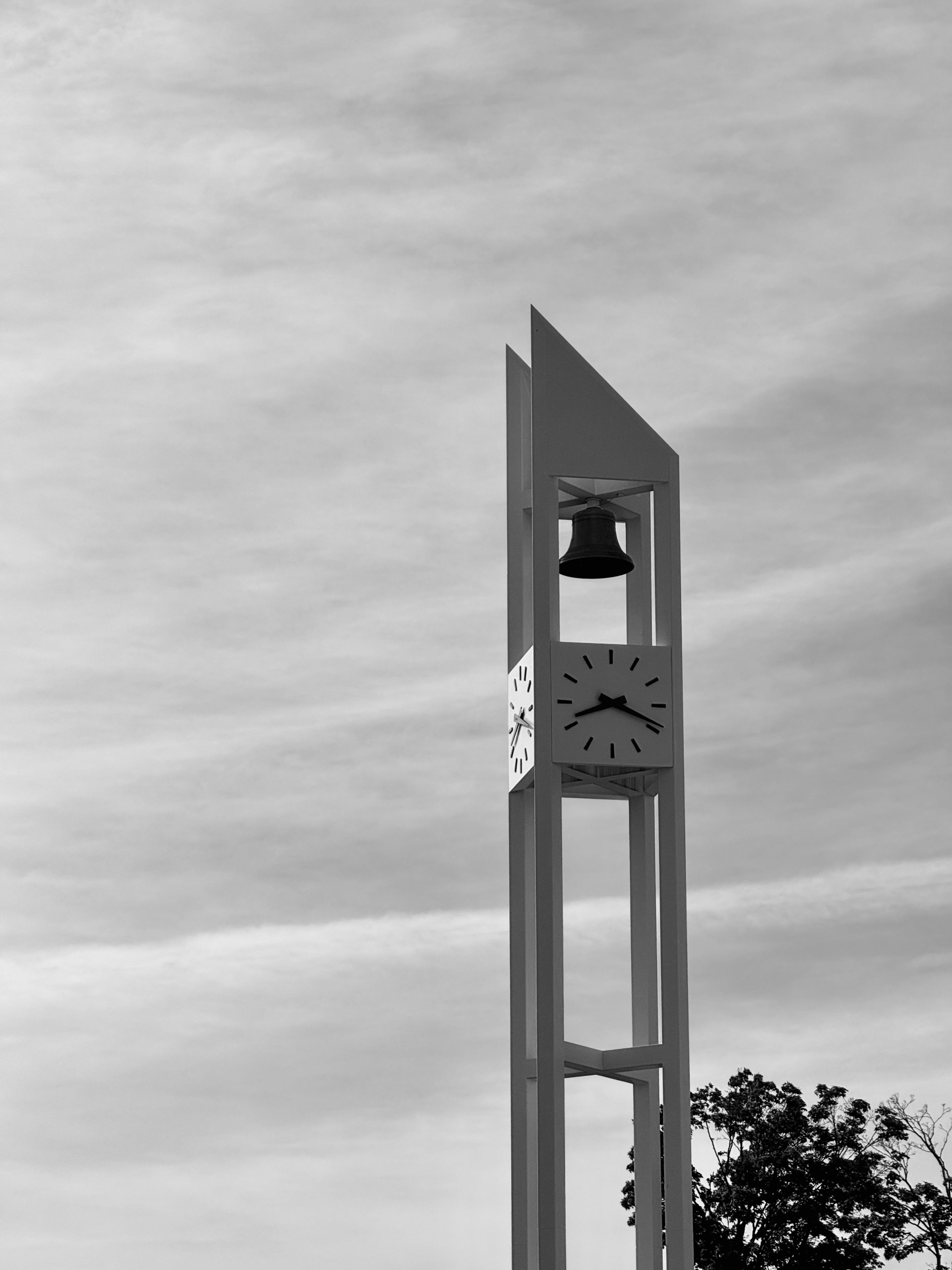 Minimalist black and white image of a clock tower with a bell set against a cloudy sky.