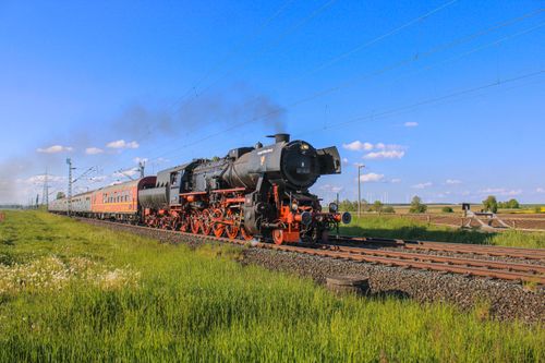 Free A vintage steam locomotive travels through picturesque countryside under a clear blue sky. Stock Photo