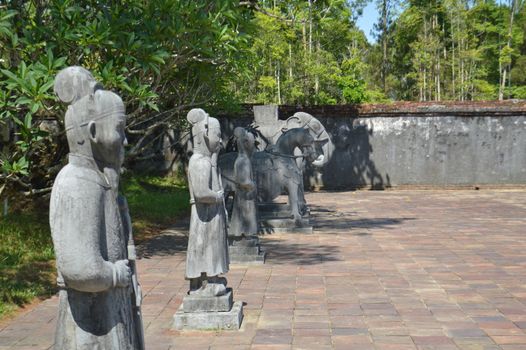 Stone sculptures line a sunlit historical courtyard, evoking a serene and ancient ambiance.