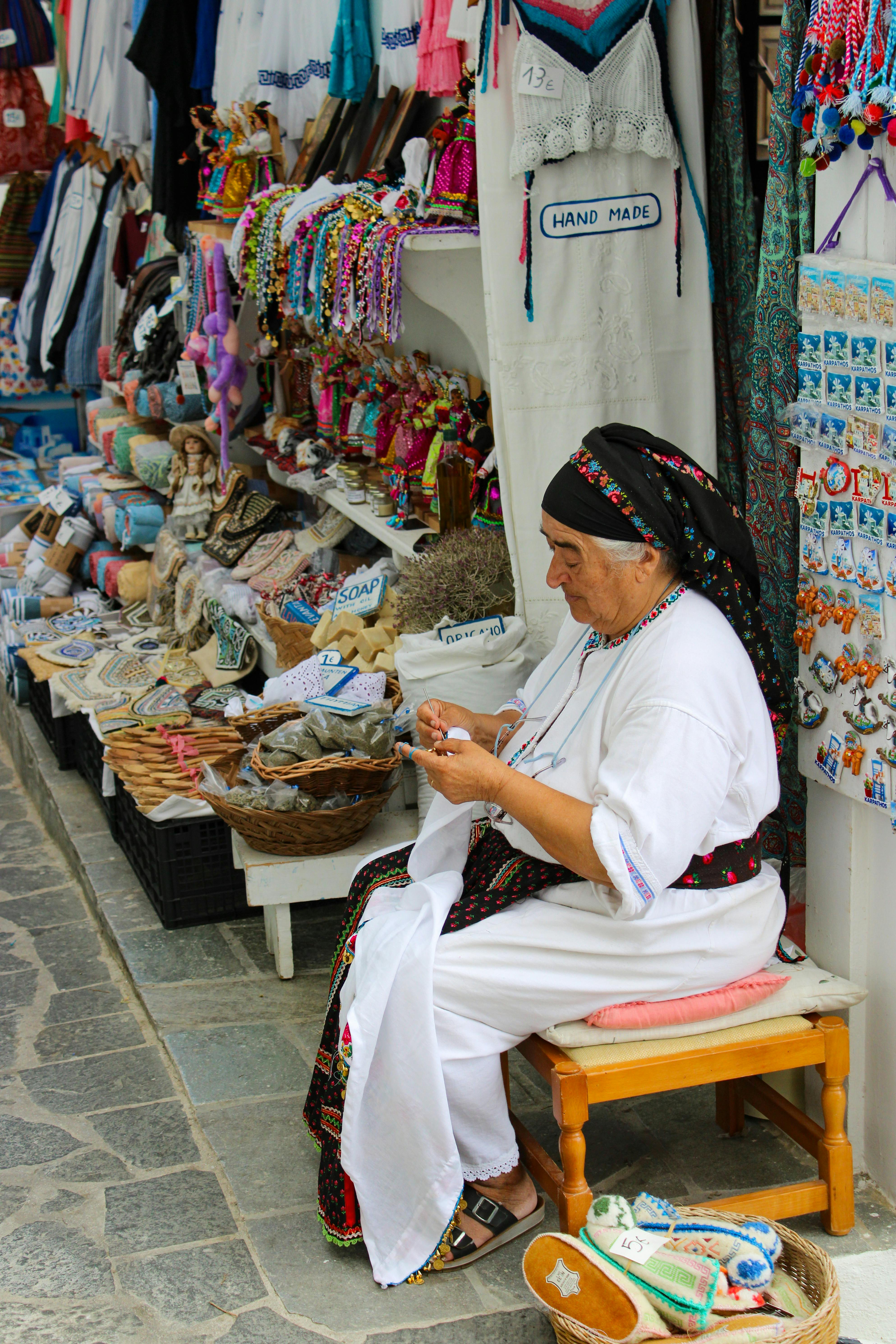 Elderly woman crafting handmade goods at a vibrant outdoor market stall.